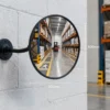 400mm Vista Flex indoor convex mirror mounted on a warehouse wall with adjustable arm and wall plate, showing warehouse aisle reflection and size dimensions
