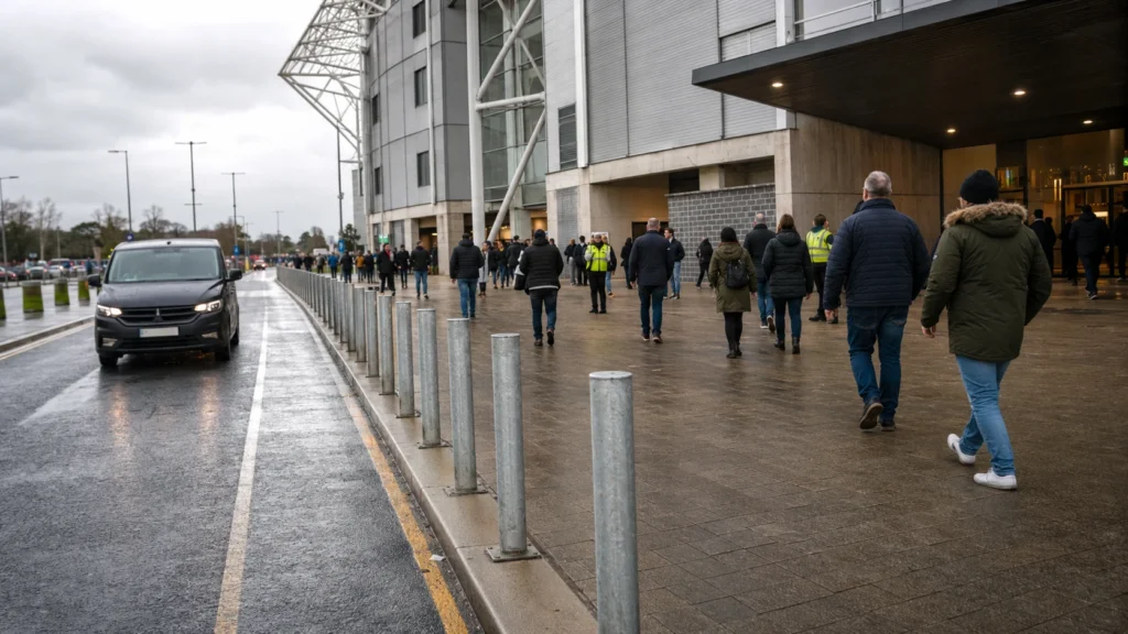 Galvanised bollards separating a stadium entrance walkway from a wet vehicle lane